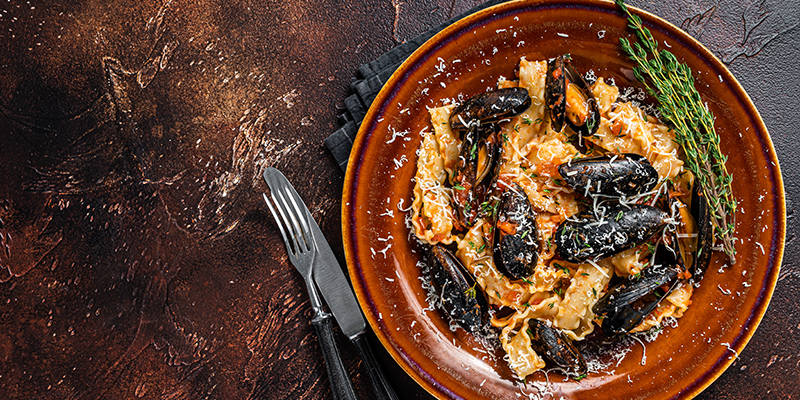 Pasta en salsa de mariscos con almejas, en un plato rústico, junto con cubiertos sobre un fondo oscuro.