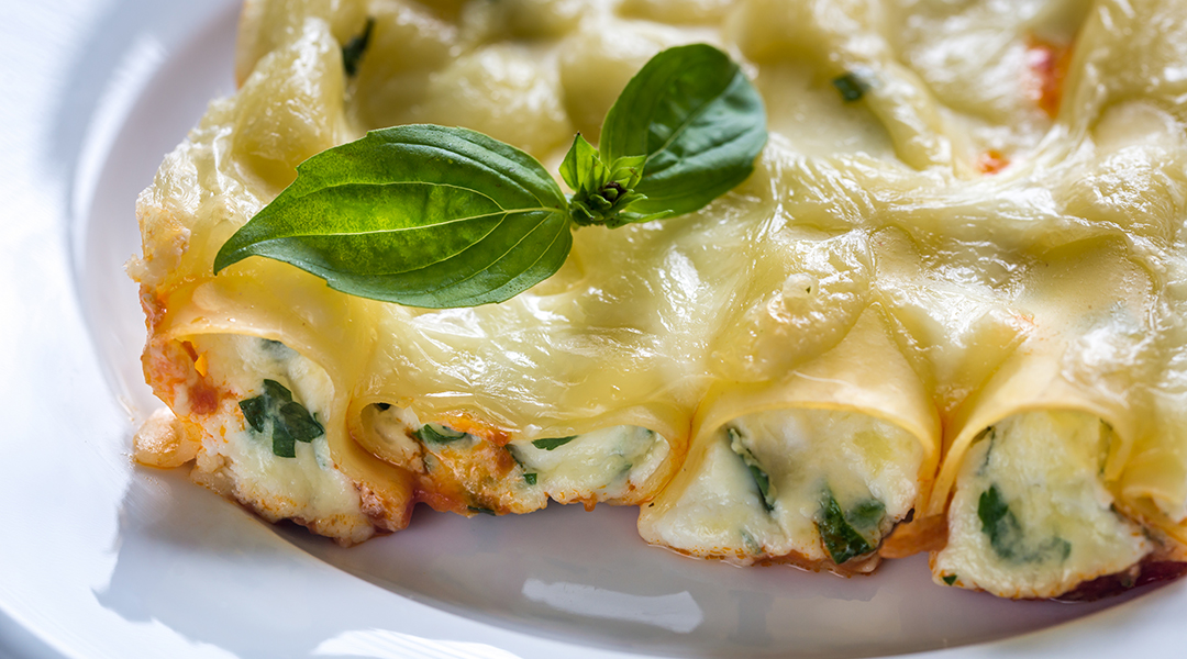 Vista de canoles de pasta rellenos con espinaca y queso sobre un plato de cerámica blanco.