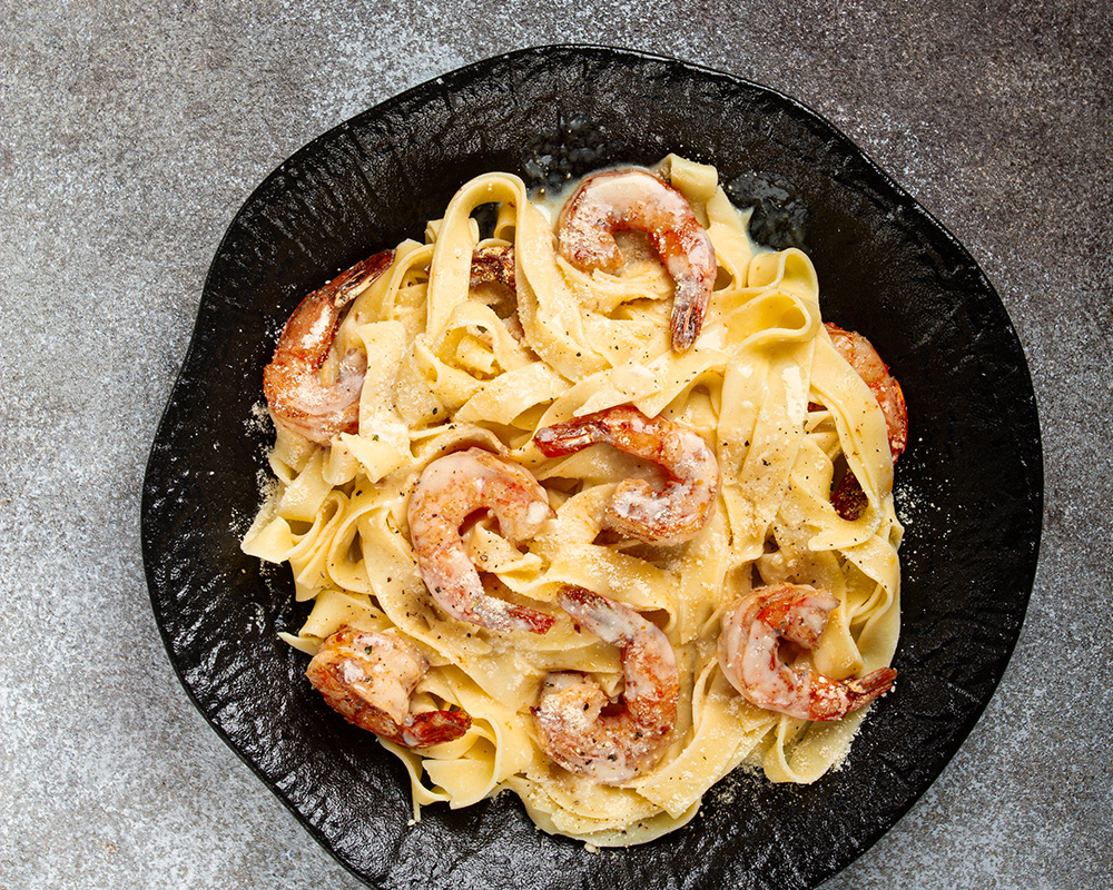 Vista superior de un plato de fettuccine con camarones en salsa cremosa, todo sobre un fondo gris.