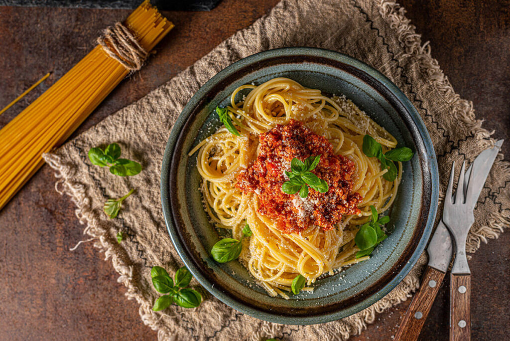 Plato de pasta a la boloñesa servido con salsa de carne, parmesano y hojas de albahaca