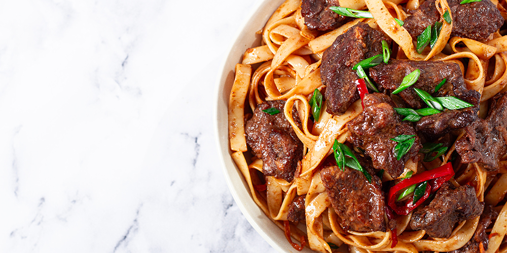 Vista superior de una plato de fettuccine con trozos de lomo saltado y especias sobre una superficie marmolizada