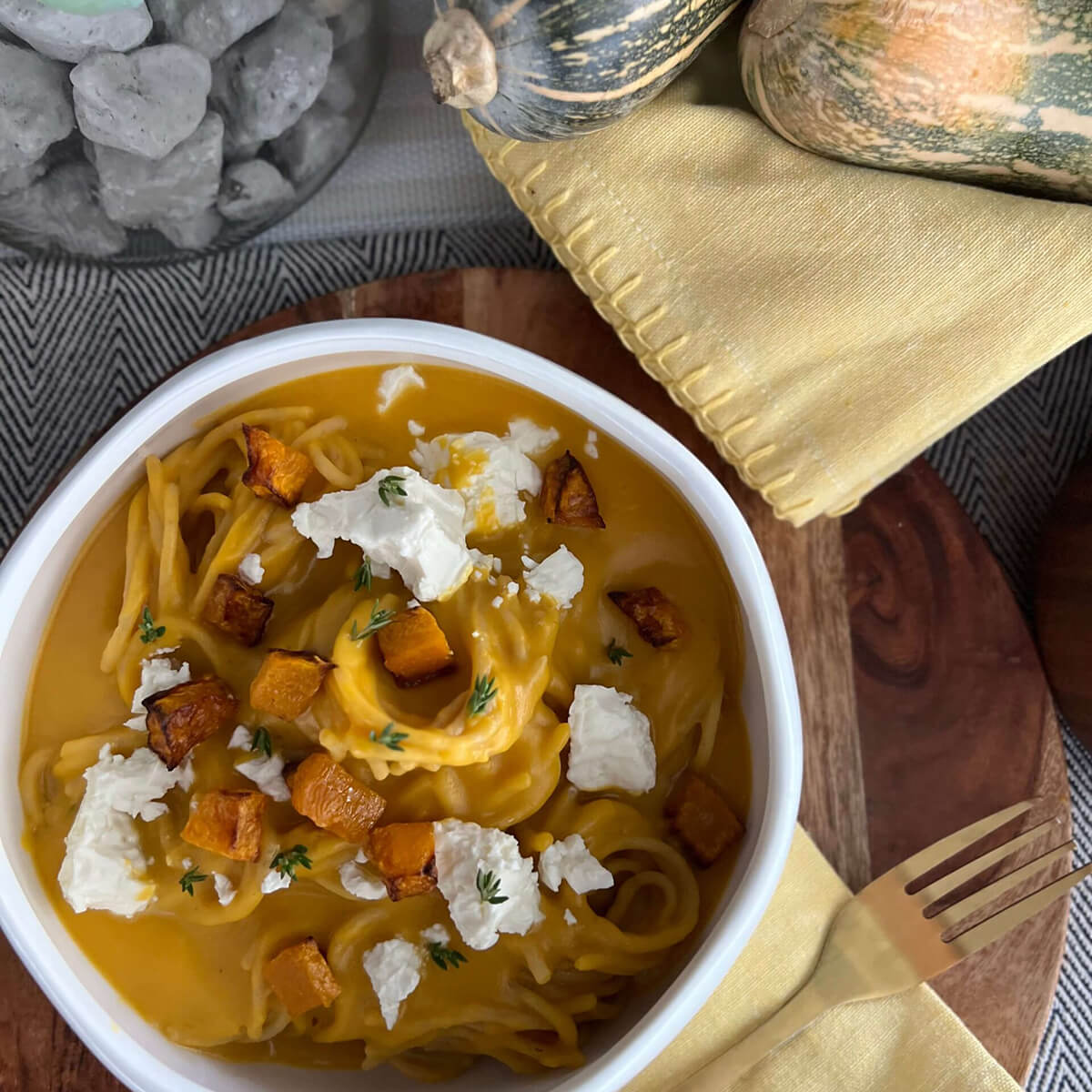 Vista superior de un plato de vermicelli integral con calabaza y mantequilla. Alrededor hay un tenedor, servilletas de tela y calabazas