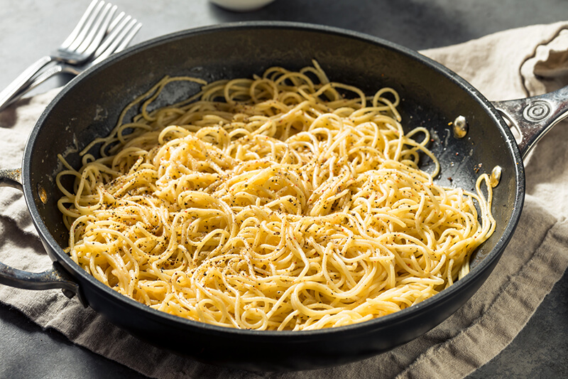 Pasta cacio e pepe en una sartén negra sobre una toalla de cocina junto con dos tenedores al lado izquierdo