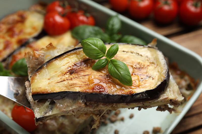Cuchara espátula de cocina, sosteniendo una Lasagna de berenjena decorada con hojas de albahaca